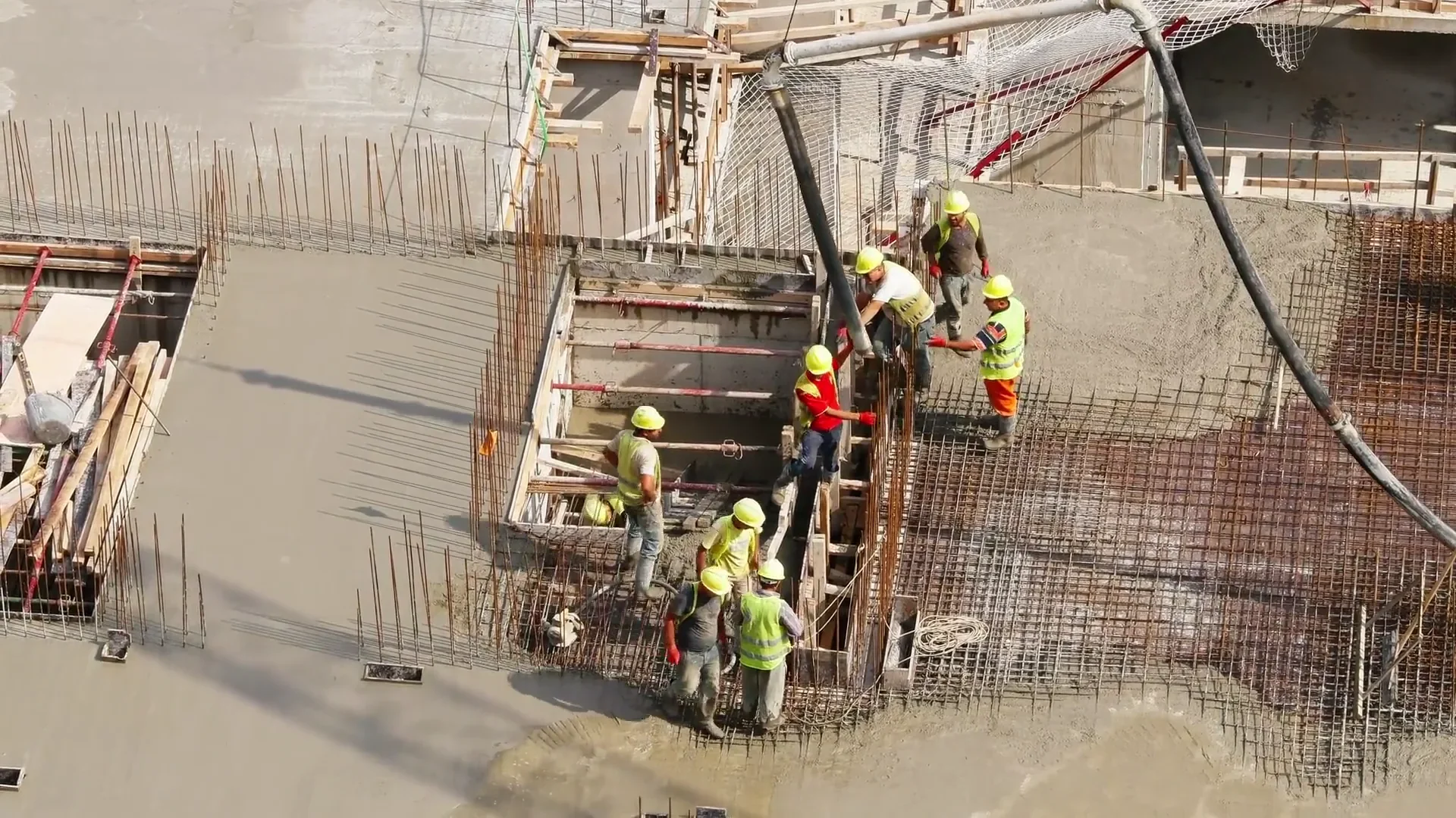 Betonare cu pompă, cofraje, armături și muncitori pe un șantier, în lumină de zi.